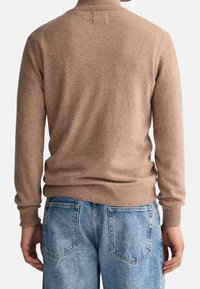 Beiger Strickpullover mit hohem Kragen, gerippten Bündchen und Saum, kombiniert mit hellblauen Jeans aus Denim mit Hintertaschen.