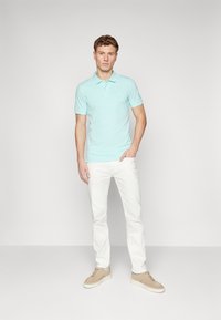 Lyseblå polo skjorte med korte ermer, med en liten logo. Kombinert med hvite bukser og beige joggesko. Enkel, ren design.