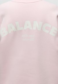 Ροζ φούτερ με τη λέξη BALANCE με μεγάλα λευκά γράμματα και τη φράση "not too much not too little" από κάτω με μικρότερα λευκά γράμματα.