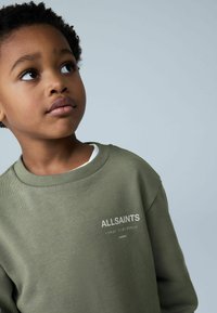 Vihreä collegepaita, jossa on resorikaulus ja hienovarainen tekstuuri. Edessä valkoinen teksti "ALLSAINTS" ja japanilaisia merkkejä.