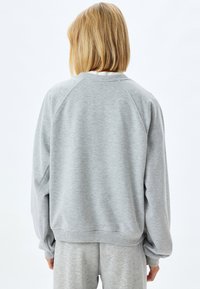 Grijze sweatshirt met een ontspannen pasvorm, geribbelde manchetten en zoom, en raglanmouwen. Glad textuur, weergegeven vanuit de achterkant. Bijpassende sweatpants zijn zichtbaar.