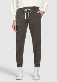 Persoon die een donkergrijze joggerbroek met een trekkoord in de taille draagt, gecombineerd met witte hoge sneakers en een crèmekleurige sweatshirt.