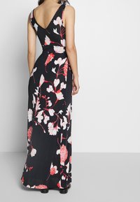Květnaté maxi šaty z černé látky, s hlubokým V-výstřihem na zádech, širokými ramínky a červenými a bílými květinovými vzory po celém povrchu. Hladká, lehká textura.
