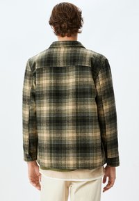 Chemise à carreaux dans des tons de vert, beige et noir ; fabriquée en tissu texturé ; dotée d'un col et de poignets boutonnés ; détail de empiècement dans le dos.