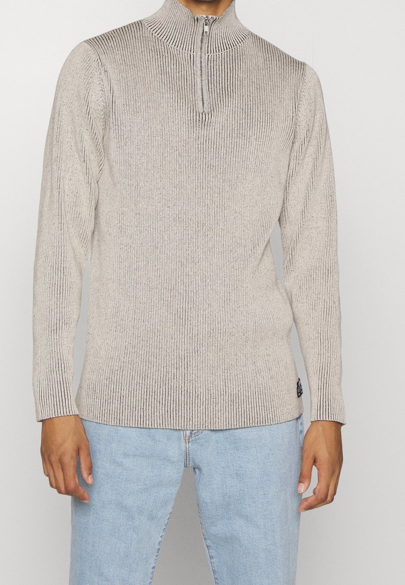 Maglione beige chiaro a coste in maglia con colletto a mezza zip e maniche lunghe, caratterizzato da una superficie texturizzata e sottili accenti screziati.