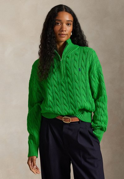 Groen kabelgebreide trui met een ritssluiting en geribde manchetten, gecombineerd met donkere broek en een bruine riem. Gestructureerde stof met een relaxte pasvorm.