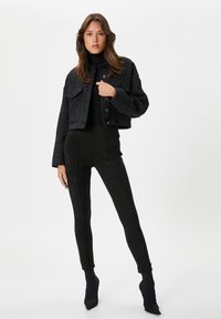 Chaqueta de denim negra cortada con detalles de costura plateada, combinada con pantalones de ante negros ajustados y botines oscuros de tacón.