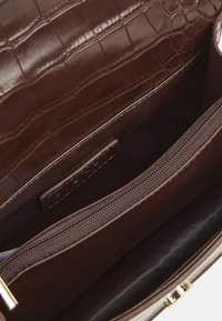 Intérieur d'un sac à main en cuir marron avec une texture crocodile, doté d'une poche zippée et d'un compartiment plat, finition lisse et quincaillerie dorée.