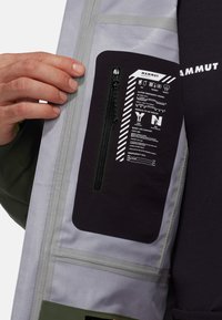 Poche intérieure en tissu noir avec une fermeture éclair, contenant des instructions de sécurité en texte blanc ; tissu gris sur les côtés ; design ergonomique.