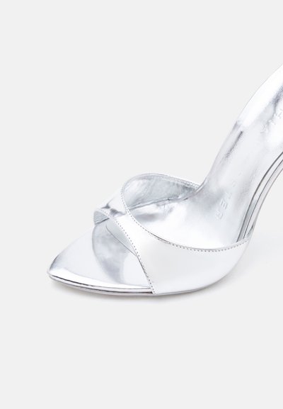 Ανοιχτό ασημί μεταλλικό πέδιλο με ψηλό τακούνι και μια μόνο λωρίδα πάνω από τα δάχτυλα, εμφανίζεται σε απλό ανοιχτό φόντο.