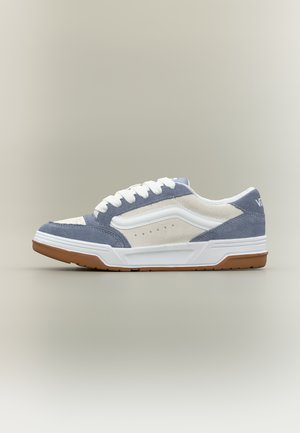 Niska tenisówka z białymi i szarymi panelami zamszowymi, białymi sznurowadłami, gumową podeszwą koloru naturalnego oraz białym paskiem po boku na neutralnym tle.