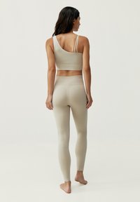 Ensemble de vêtements de sport beige comprenant un crop top asymétrique et un legging taille haute avec un motif texturé. Design minimaliste, construction sans couture.