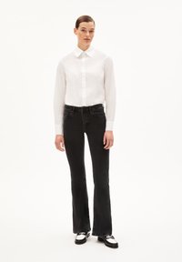 White button-up shirt, black flared jeans, and black shoes with metallic accents. Smooth fabric, tailored fit, and structured collar.