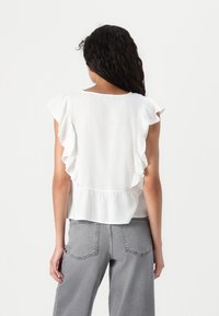 Witte linnen blouse met vleermuismouwen en een gerimpelde achterkant. Gekoppeld aan lichtgrijze wijde jeans. Zachte textuur, eenvoudig en elegant ontwerp.