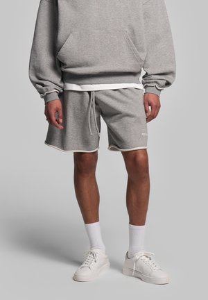 Felpa grigia con tasca frontale, abbinata a pantaloni shorts coordinati con dettagli bianchi. Completato con sneaker bianche e calze corte.