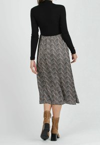 Haut noir à manches longues en côtes associé à une jupe mi-longue avec un motif en chevron dans des tons terreux. Porté avec des bottines en daim beige.