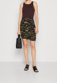 Svart linne kombinerat med en figurnära kjol som går till knäna och har ett mönster i grönt och svart med vågor, kompletterat med en svart handväska och öppna skor.