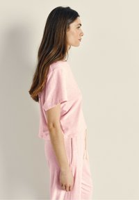 Roze cropped top met korte mouwen en zijslitsen, gecombineerd met bijpassende joggerbroeken met een elastische tailleband en trekkoord.