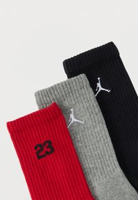 Τρία ζευγάρια ριγέ κάλτσες σε κόκκινο, γκρι και μαύρο, με το μαύρο αριθμό "23" στην κόκκινη κάλτσα και λευκά λογότυπα Jumpman στις γκρι και μαύρες κάλτσες.