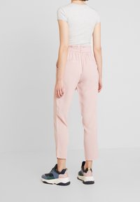 Pantalons rose clair, fuselés, avec une taille élastique, des poches latérales et un tissu lisse, associés à des baskets de sport multicolores.