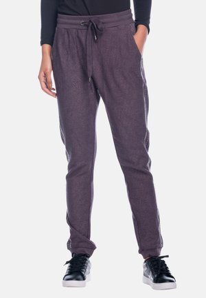 Lila Jogginghosen mit strukturiertem Finish, Kordelzugbund, seitlichen Taschen und eng anliegenden Bündchen, kombiniert mit schwarzen Sneakern.