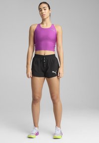 Lilla sportlik crop-top, mustad lühikesed püksid stringiga ja mitmevärvilised jooksukingad, millel on valged, rohelised ja lillad aktsendid.