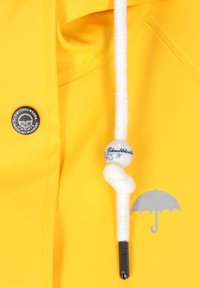 Geltonas vandeniui atsparus švarkas su baltu raišteliu, kuriame yra dekoratyvinis karoliukas. Įtrauktas sidabrinis skėčio logotipas ir juodas metalinis mygtukas.