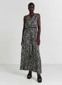 Blumen-Jumpsuit in Marineblau mit weißen Mustern, mit ärmellosem Design, weitem Bein und figurnaher Taille. Ergänzt durch klobige schwarze Absätze.
