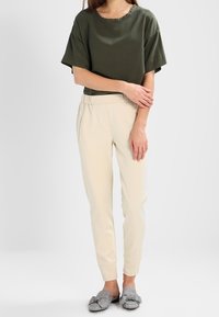 Olive green short-sleeve top, beige tapered pants, and gray checkered slippers. The outfit features a relaxed fit and soft fabric textures.