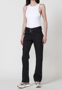 Pantalones cargo negros con bolsillos, un cinturón y corte recto; combinados con un body sin mangas blanco y zapatillas multicolores.