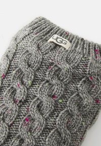 Guanto grigio lavorato a maglia con un motivo a treccia, decorato da macchie colorate di rosa e verde. Presenta un'etichetta con il logo UGG nella parte superiore.