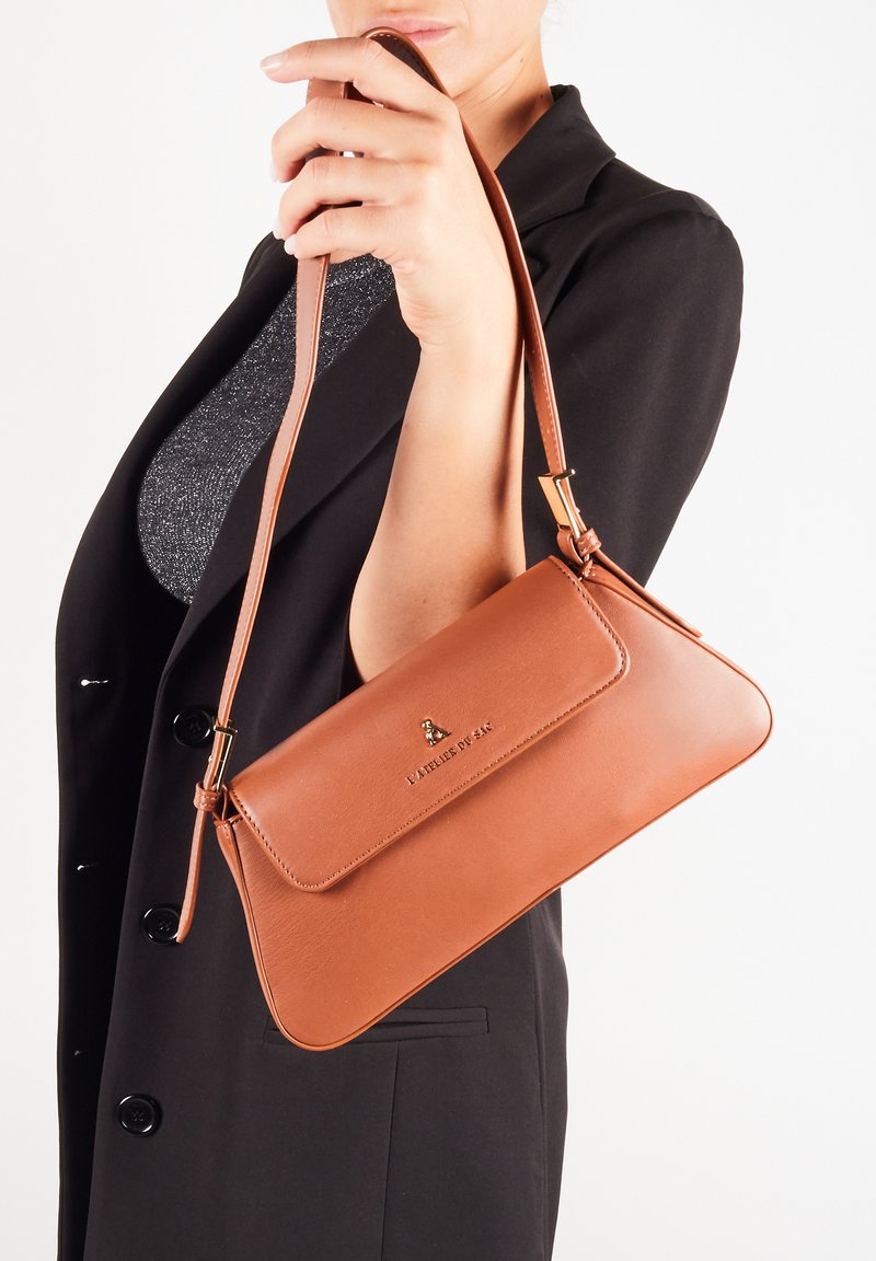 Brązowa skórzana torebka o płaskim designie, z odpinanym paskiem i magnetycznym zapięciem na klapę. Zawiera delikatne logo umieszczone z przodu.