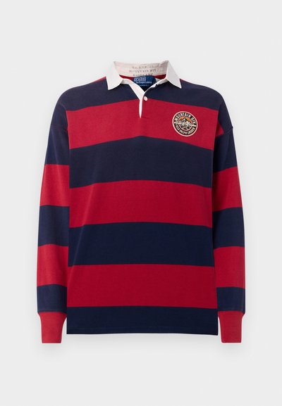 Ilgais rankovės polo marškinėliai raudonos ir mėlynos horizontalios juostelės, su balta apykakle ir apvaliu siuvinėtu logotipu krūtinėje.