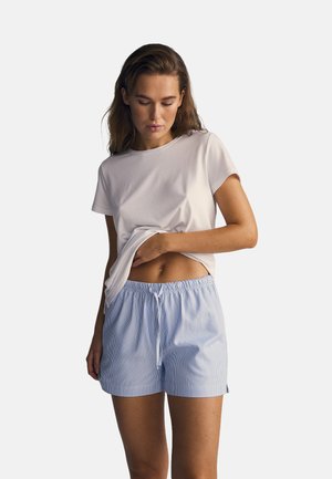 Hvid bomuld t-shirt med korte ærmer, parret med blå-stribede bomuldsshorts med elastisk talje og snor.
