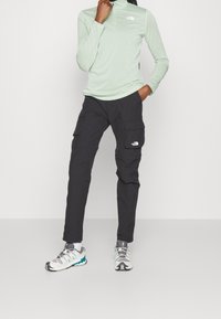 Jasnozielona bluzka z długim rękawem i kołnierzem z półzamkiem. Czarne spodnie cargo z dwiema bocznymi kieszeniami. Szare i niebieskozielone buty sportowe.