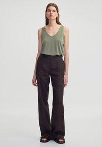 Olijfgroene mouwloze top met V-hals, gecombineerd met hooggetailleerde, wijde bruine broek, voorzien van subtiele verticale streepjes en instap sandalen.