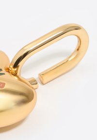 Lucchetto a forma di cuore in oro con finitura lucida, caratterizzato da un gancio curvo e un piccolo accento rosa sul corpo. Texture liscia.