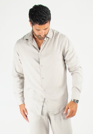 Chemise à boutons grise claire à manches longues en tissu doux et texturé. Elle présente un col décontracté et de subtils accents de boutons.