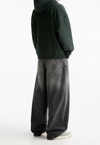 Felpa verde scuro con un taglio comodo, abbinata a jeans grigi larghi e sbiaditi con più tasche e dettagli della cucitura ben visibili.