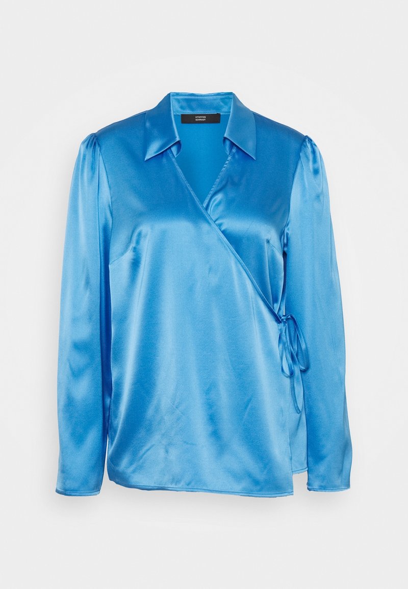 Blouse portefeuille en satin bleu avec manches longues, col et fermeture à nouer sur le côté, sur fond uni.