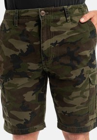 Pantalones cortos de camuflaje en tonos de verde, marrón y negro; cuentan con un cierre de botón, bolsillos laterales y un corte relajado con dobladillo cosido.