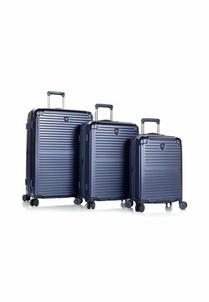 Trois valises rigides bleu marine avec poignées télescopiques et quatre roues, disposées de la plus grande à la plus petite sur un fond blanc.