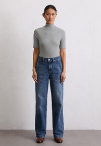 Szary, krótki golf z rękawami, zestawiony z dżinsami z wysokim stanem i szerokimi nogawkami w kolorze niebieskim, które mają przednie kieszenie i zapięcie na guzik.