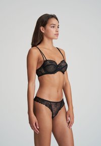 Schwarzes Spitzen-BH- und String-Set mit Blumenmustern, durchscheinendem Material und gewellten Kanten. Verstellbare Träger am BH für eine optimale Passform.
