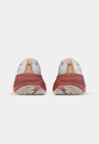 Des chaussures de course avec une tige en maille blanche et des accents roses, une semelle intermédiaire rouge, une semelle extérieure en caoutchouc texturé, et une languette au talon pour un enfilage facile.