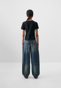 Black short-sleeve t-shirt paired with wide-leg dark blue jeans. Jeans feature a faded wash, two back pockets, and a leather patch.