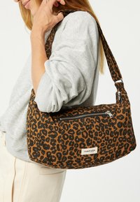 Leopardenmuster Schultertasche aus braunem und schwarzem Stoff, mit einem Reißverschlussfach, breitem Griff und dezentem Markenlabel auf der Vorderseite.