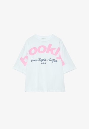 Witte oversized T-shirt met roze "Brooklyn" tekst diagonaal en blauwe "Crown Heights, New York U.S.A" tekst gecentreerd aan de voorkant.
