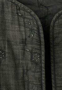 Țesătură gri închis cu broderie florală subtilă și mărgele negre mici, evidențiind textura și detaliile cusăturii la margine.