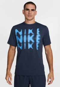 Navy blue cotton t-shirt featuring a prominent light blue zigzag pattern text across the front. Short sleeves and round neck design.